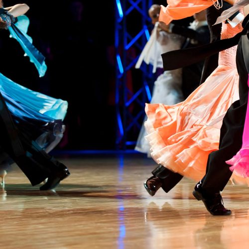 Tanzpaare auf der Fläche während eines Standardturnieres. Die Damen in farbigen Kleidern werden von ihren Herren durch die Choreografien geführt.
